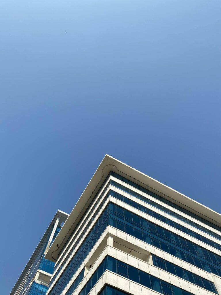 Low angle view of a modern office building with glass windows in Gurugram, India against a clear blue sky.